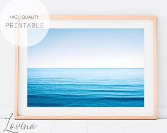 May include: A framed photograph of a blue ocean with a light blue sky in the background. The ocean is calm and the waves are small. The photo is framed in a light wood frame.