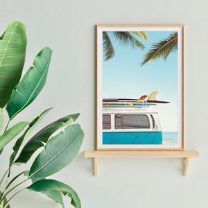 May include: A framed print of a blue vintage van with surfboards on the roof, parked on a beach with palm trees in the background.