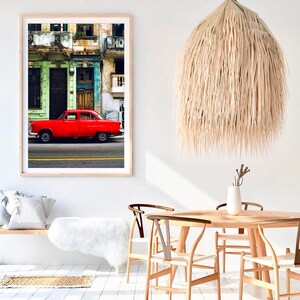 May include: A framed photograph of a red vintage car parked in front of a colorful building in Havana, Cuba. The building has green and blue paint and a wooden door. The car is a classic American model with chrome accents.
