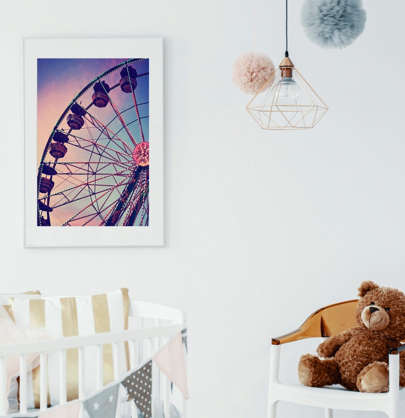 Puede incluir: Una impresi&oacute;n enmarcada de una colorida noria contra un cielo de puesta de sol rosa y morado. La impresi&oacute;n est&aacute; colgada en una pared blanca en una guarder&iacute;a con una cuna y un oso de peluche sentado en una silla.