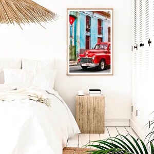 May include: A red vintage car parked in front of a blue and green building with a Cuban flag hanging from the building. The car has chrome accents and whitewall tires.