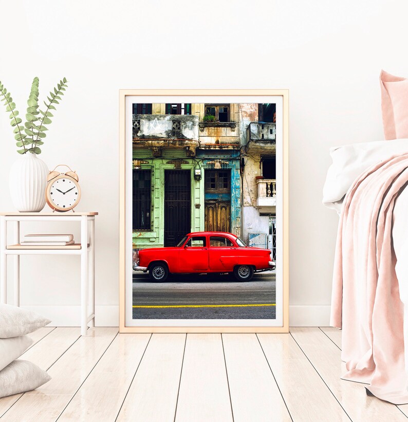 May include: A vintage red car parked in front of a colorful building with green, blue, and yellow accents. The building has multiple windows and balconies.