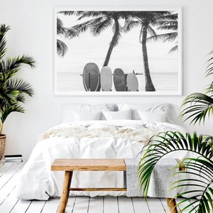 K&ouml;nnte beinhalten: Schwarzwei&szlig;foto von Surfbrettern, die an Palmen an einem Strand lehnen. Das Foto ist gerahmt und h&auml;ngt &uuml;ber einem wei&szlig;en Bett mit einer Holzbank.