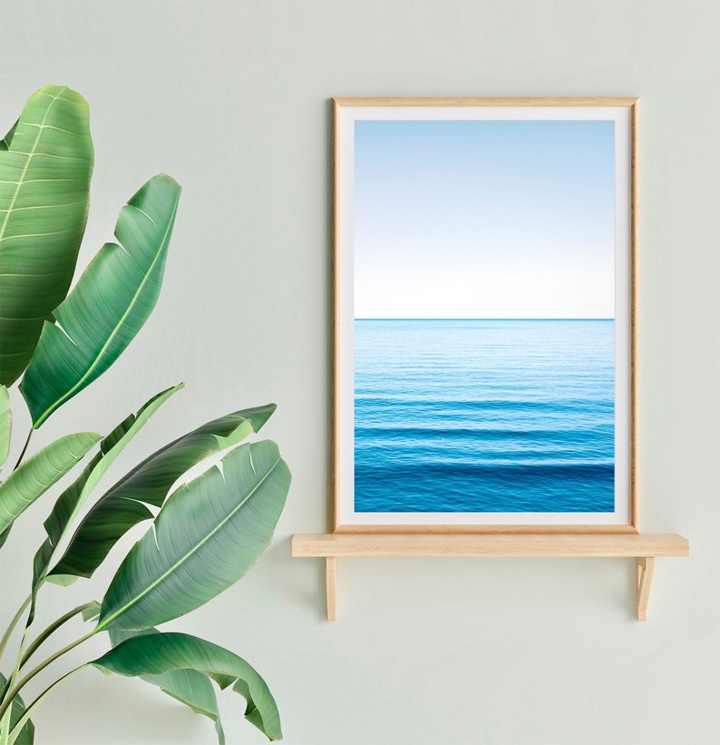 May include: A framed photograph of a blue ocean with a light blue sky above. The photograph is on a wooden shelf against a light green wall.