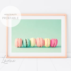 Puede incluir: Una fila de seis macarons de color pastel sobre un fondo verde claro. Los macarons están dispuestos en línea, con los colores pasando del rosa al amarillo.