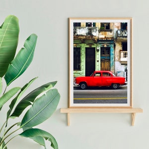 May include: A vintage red car parked in front of a colorful building with peeling paint. The building has green, blue, and yellow accents. The car is a classic American sedan with chrome accents.