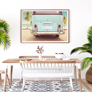 Pode incluir: Uma fotografia emoldurada de uma van vintage azul claro com uma placa que diz "HELLO SUMMER" estacionada em uma praia com palmeiras ao fundo.