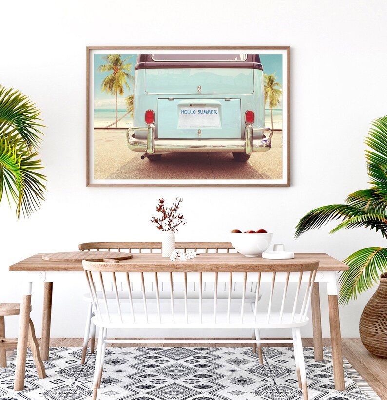 Pode incluir: Uma fotografia emoldurada de uma van vintage azul claro com uma placa que diz "HELLO SUMMER" estacionada em uma praia com palmeiras ao fundo.