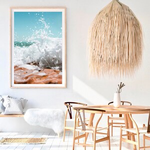 May include: A framed print of a crashing ocean wave with a light wood frame. A woven pendant light hangs from the ceiling. The room features a wooden table and chairs, a white bench, and a fluffy white rug.