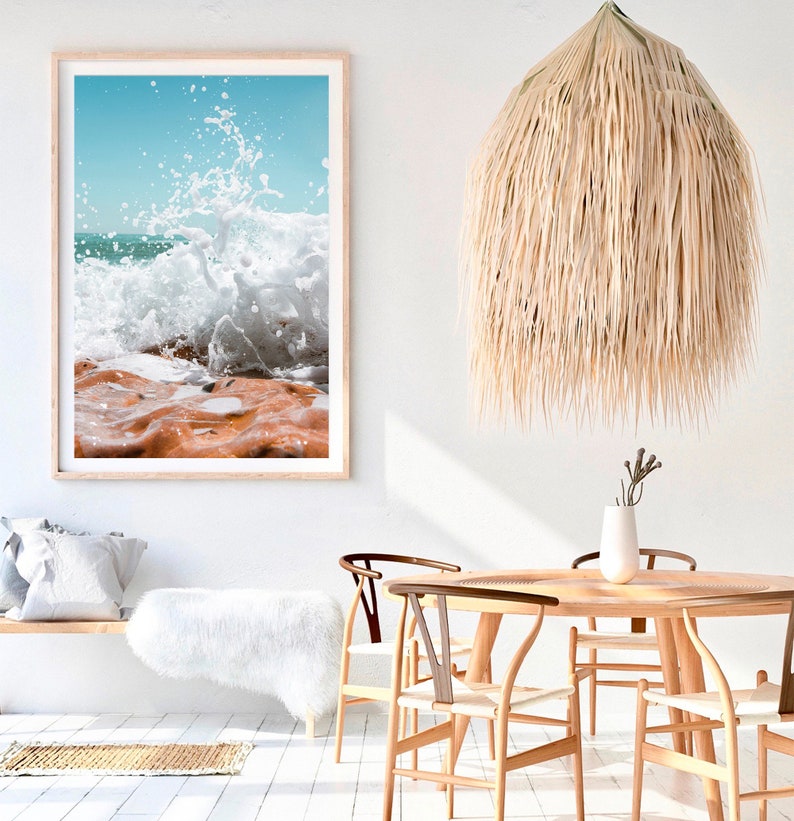 May include: A framed print of a crashing ocean wave with a light wood frame. A woven pendant light hangs from the ceiling. The room features a wooden table and chairs, a white bench, and a fluffy white rug.