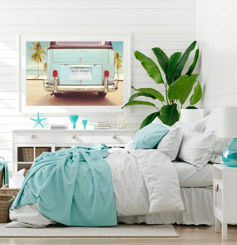 Pode incluir: Um quarto branco com uma cama, uma c&ocirc;moda branca e uma impress&atilde;o emoldurada de uma van vintage azul com as palavras "Hello Summer" na placa. A van est&aacute; estacionada em uma praia com palmeiras ao fundo.