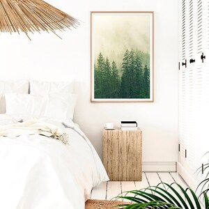 May include: A white bedroom with a bed, a wooden nightstand, a framed print of a foggy forest, and a woven ceiling lamp.