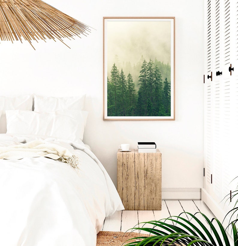 May include: A white bedroom with a bed, a wooden nightstand, a framed print of a foggy forest, and a woven ceiling lamp.