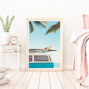 May include: A framed print of a blue vintage van with surfboards on the roof, parked on a beach with palm trees in the background.