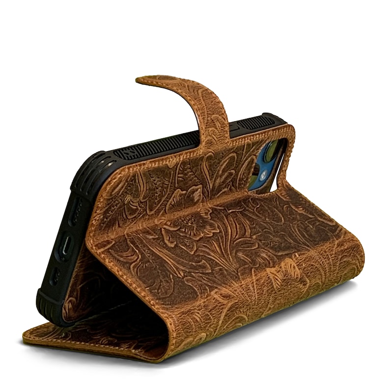May include: A brown leather phone case with a floral embossed design. The case has a flap that folds over the phone and a strap to keep it closed.