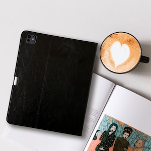 May include: A black tablet case with a textured finish, a silver clasp, and a coffee cup with a heart-shaped design in the foam. An open magazine with colorful illustrations is also visible.