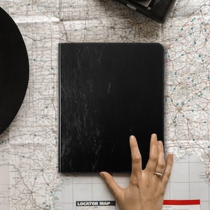 May include: Black leather-bound journal with a textured cover. The journal is lying flat on a map.