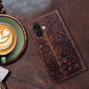 May include: A brown leather phone case with an embossed floral design. The case has a cutout for the camera lens.