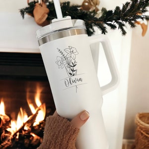 May include: White stainless steel travel mug with a black floral design and the name "Olivia" printed on it. The mug has a handle and a lid with a straw.