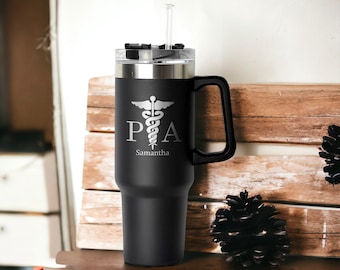 Puede incluir: Taza de viaje de acero inoxidable negro con asa negra y pajita. La taza tiene un diseño grabado en blanco de un caduceo médico con las letras "PA" y el nombre "Samantha" debajo.