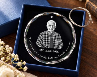 Op de afbeelding: Een rond gedenk-ornament van helder glas met een gegraveerd portret van een persoon in een geruit overhemd met stropdas. De tekst luidt DAD (1938 - 2025) en Your wings were ready but our hearts were not. Inclusief een zilverkleurig koord.