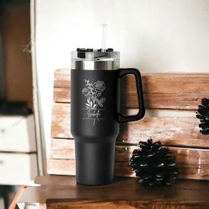 May include: Black stainless steel travel mug with a black handle and a clear lid. The mug has a floral design and the name "Isabel" engraved on the side.