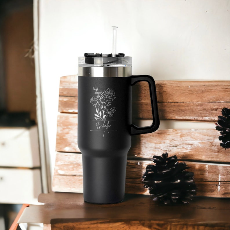 May include: Black stainless steel travel mug with a black handle and a clear lid. The mug has a floral design and the name "Isabel" engraved on the side.