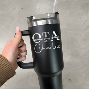 Pu&ograve; includere: Tazzina da viaggio in acciaio inossidabile nero con manico. La tazza ha un'iscrizione bianca che recita "OTA Occupational Therapy Assistant Charles".