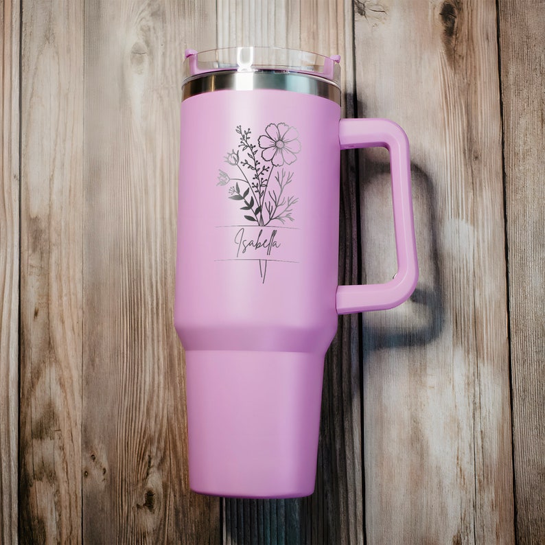 May include: A purple stainless steel travel mug with a black floral design and the name "Isabella" engraved on it.