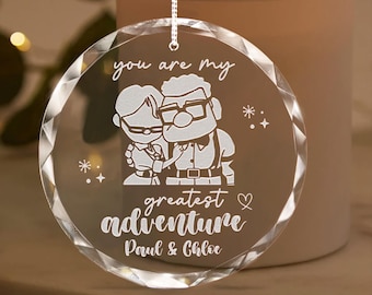 May include: A clear crystal ornament with a white etched design of a cartoon couple, the text "You are my greatest adventure" and the names "Paul & Chloe".