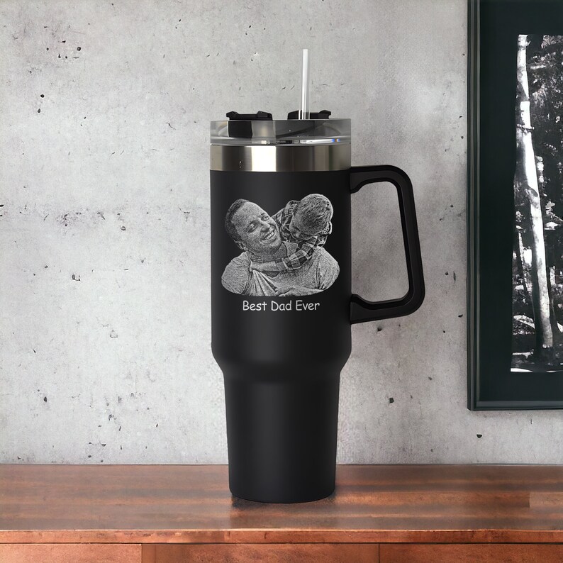 May include: Black stainless steel travel mug with a black handle. The mug has a photo of a father and child engraved on the front with the text "Best Dad Ever".