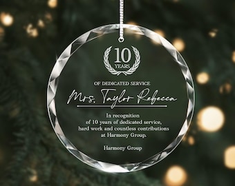 May include: A clear, round glass ornament with a faceted edge, suspended by a silver chain. The ornament features the text "10 YEARS OF DEDICATED SERVICE" and "Mrs. Taylor Rebecca" with additional text recognizing 10 years of service at Harmony Group.