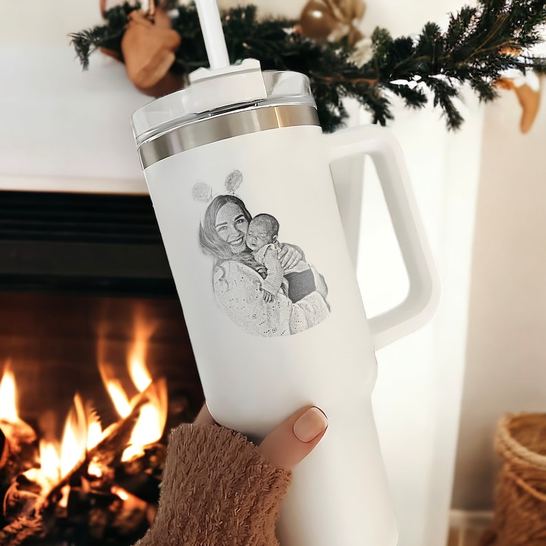 May include: White travel mug with a handle and a black and white photo of a mother and child engraved on the side.