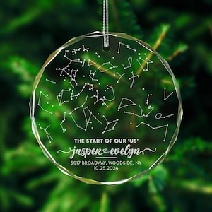 May include: A clear glass ornament with a constellation design and the text "THE START OF OUR 'US' jasper evelyn 5017 BROADWAY, WOODSIDE, NY 10.25.2024".