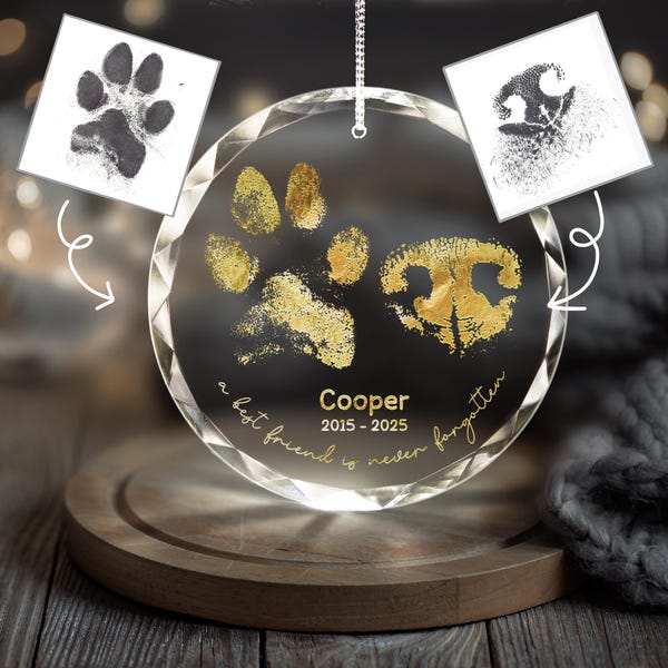 May include: A clear, round crystal ornament with gold paw prints and a dog nose print. The name "Cooper" and dates 2015-2025 are below the prints. The text "a best friend is never forgotten" is written around the edge.
