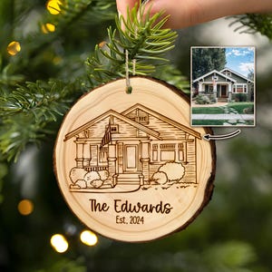 May include: A wooden ornament with a laser-engraved illustration of a house. The ornament is round and has a hole at the top for hanging. The text "The Edwards Est. 2024" is engraved below the house.
