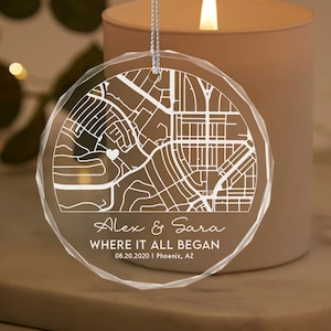 May include: A clear glass ornament with a white outline of a city map and a small heart in the center. The text "Alex & Sara Where It All Began 08.20.2020 | Phoenix, AZ" is printed below the map.