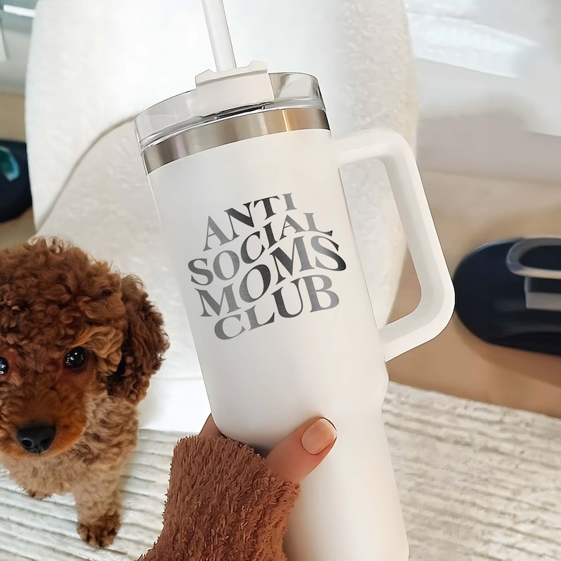 以下が含まれることがあります： 黒の取っ手と「Anti Social Moms Club」という白黒のグラフィックが描かれた白いステンレス製のトラベルマグです。
