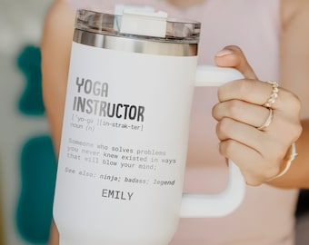 May include: White insulated tumbler with a handle and a clear lid. The tumbler has the words "YOGA INSTRUCTOR" printed on it, along with a definition and the name "EMILY". The tumbler is designed to keep beverages hot or cold.
