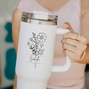 May include: White stainless steel travel mug with a black floral design and the name "Isabella" printed on it.