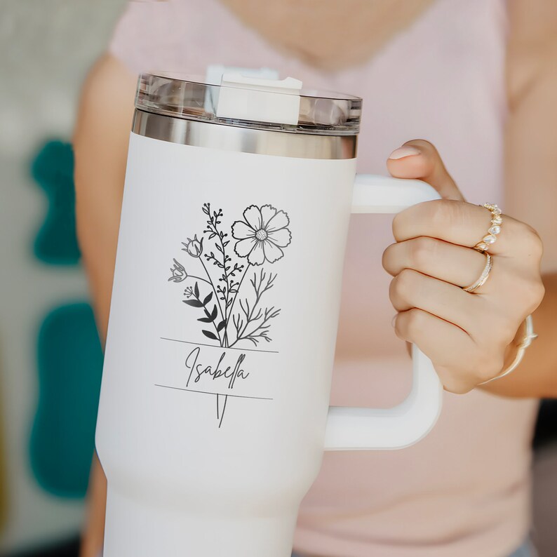 May include: White stainless steel travel mug with a black floral design and the name "Isabella" printed on it.