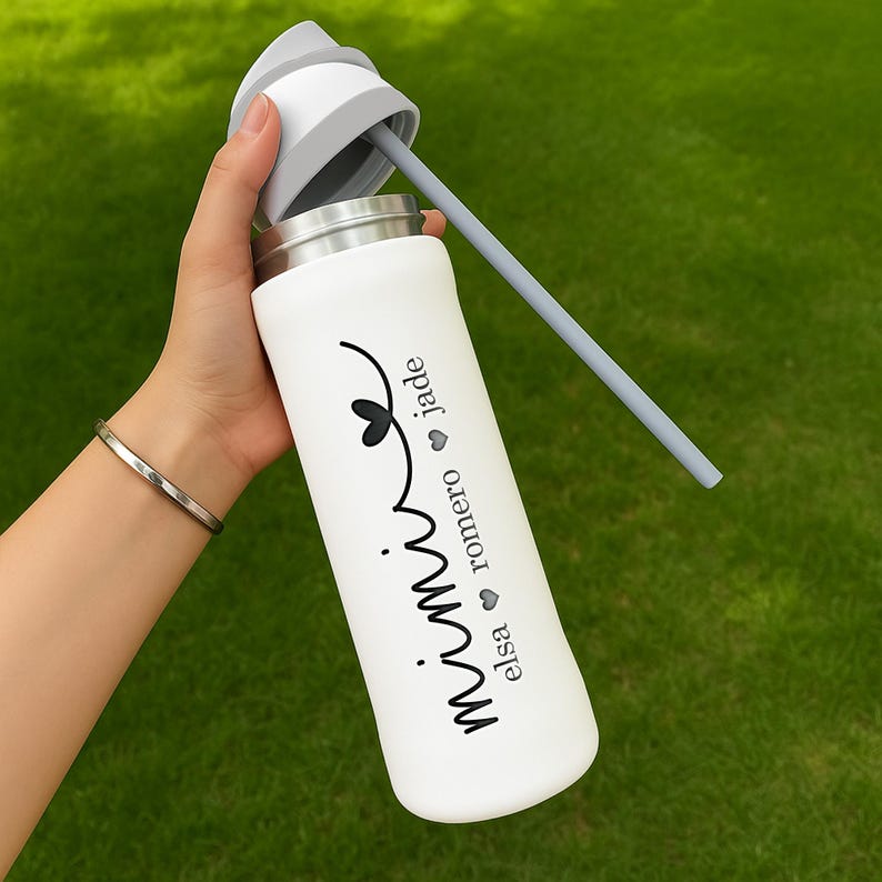 May include: White insulated water bottle with a gray lid and straw. The bottle features the word "Mimi" in a script font, with the names "Elsa", "Romero", and "Jade" below. The bottle is held against a green background.