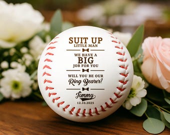 May include: A white baseball with red stitching and text that reads "SUIT UP LITTLE MAN, WE HAVE A BIG JOB FOR YOU, WILL YOU BE OUR Ring Bearer? Jimmy 12.10.2025". The baseball is a wedding proposal item.