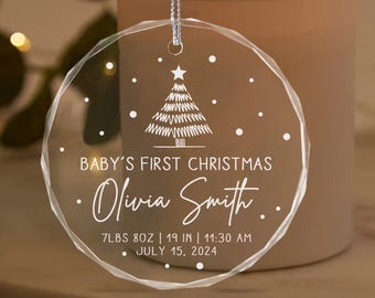 May include: A clear glass Christmas ornament with a white outline of a Christmas tree and snowflakes. The ornament is personalized with the text "BABY'S FIRST CHRISTMAS Olivia Smith. 7LBS 8OZ | 19 IN | 11:30 AM JULY 15, 2024".