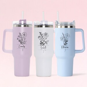 May include: Three stainless steel travel mugs with lids and straws. The mugs are in lavender, white, and light blue. Each mug has a floral design and a name on it: Emily, Isabella, and Olivia.