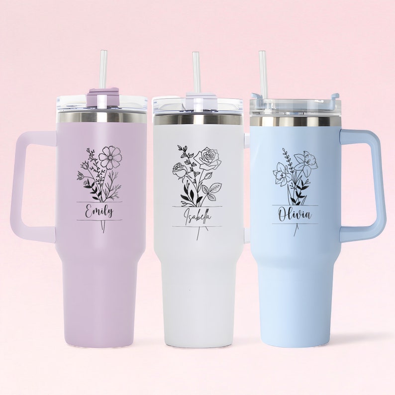 May include: Three stainless steel travel mugs with lids and straws. The mugs are in lavender, white, and light blue. Each mug has a floral design and a name on it: Emily, Isabella, and Olivia.