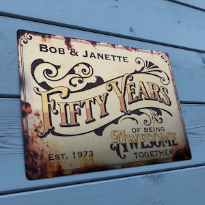 May include: A rusty metal sign with gold lettering that reads "Bob & Janette Fifty Years of Being Awesome Together" and "Est. 1973".