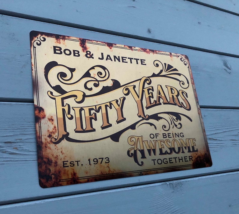 May include: A rusty metal sign with gold lettering that reads "Bob & Janette Fifty Years of Being Awesome Together" and "Est. 1973".