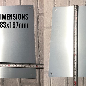 May include: A silver metal sign with rounded corners and four holes for hanging. The sign has the text "DIMENSIONS 283x197mm" printed in black.