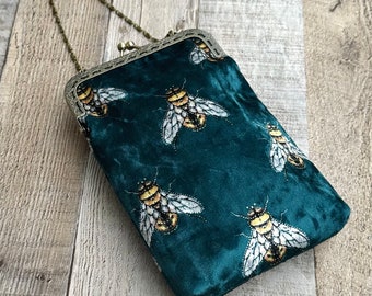 Könnte beinhalten: Eine tealblaue Samt-Handtasche mit einer goldenen Kettenriemen und einem Verschluss. Die Tasche ist mit einem sich wiederholenden Muster von Bienen verziert.
